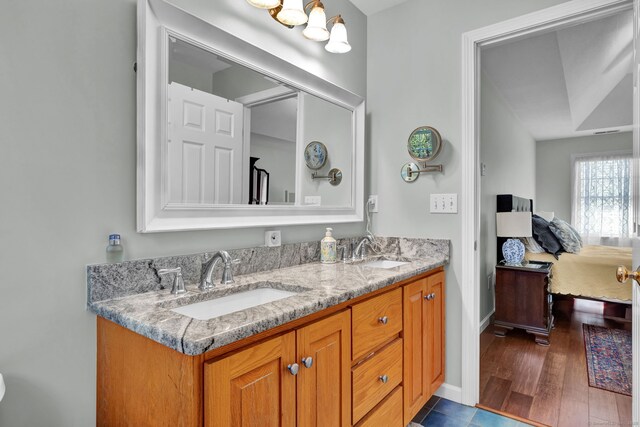 ensuite bathroom with connected bathroom, double vanity, baseboards, and a sink