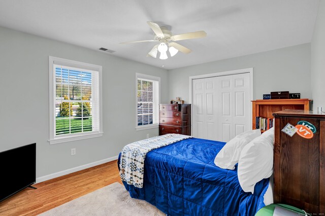 bedroom with a ceiling fan, baseboards, wood finished floors, visible vents, and a closet