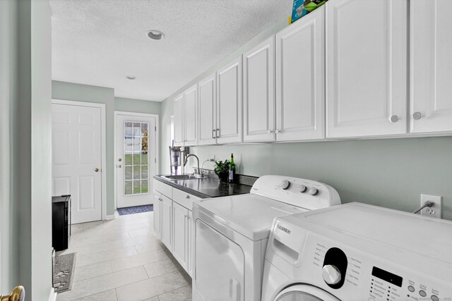 washroom featuring cabinet space, a sink, a textured ceiling, light tile patterned floors, and washer and clothes dryer