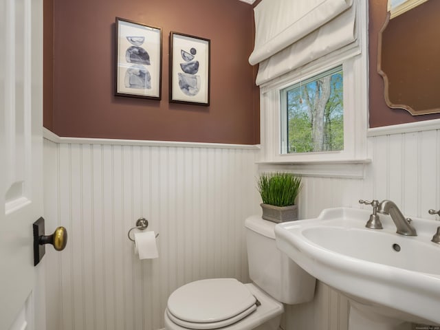 half bath with a sink, wainscoting, and toilet