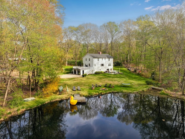 rear view of property featuring a lawn, a chimney, a deck with water view, and a wooded view