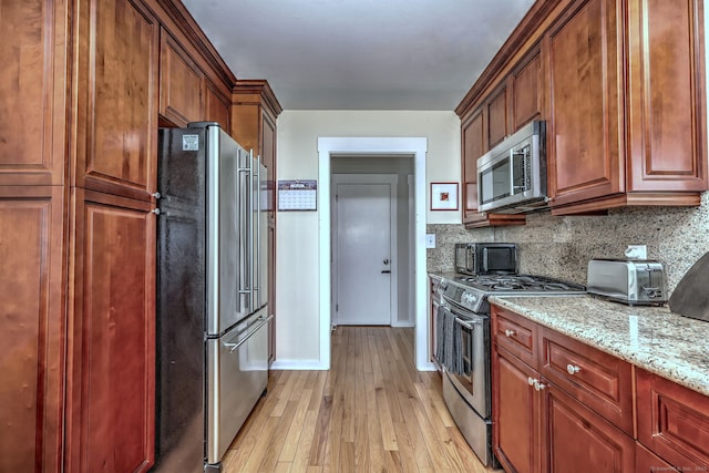 kitchen with a toaster, light stone countertops, tasteful backsplash, light wood-style flooring, and appliances with stainless steel finishes