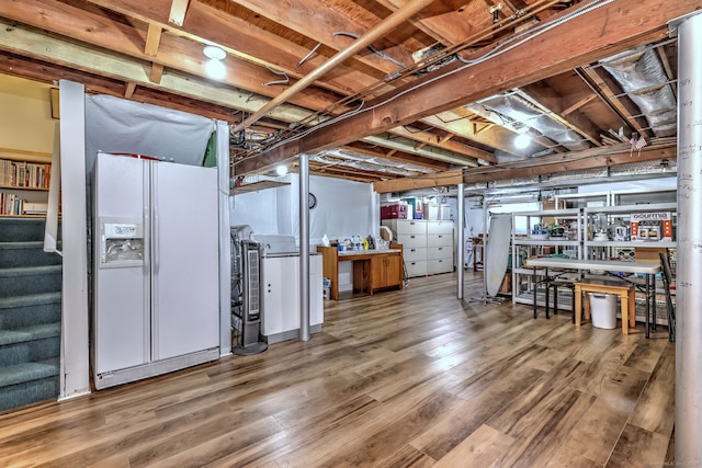 unfinished below grade area with stairs, wood finished floors, and white refrigerator with ice dispenser