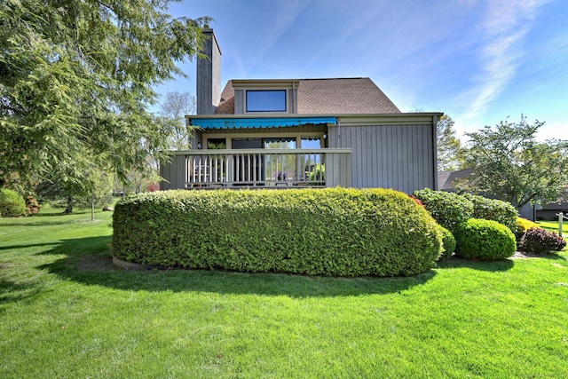 rear view of house with a lawn, board and batten siding, a chimney, and a balcony