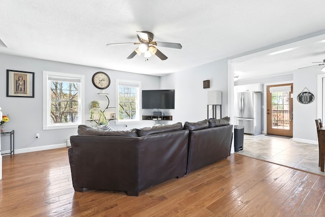 living area with wood-type flooring, a ceiling fan, and baseboards