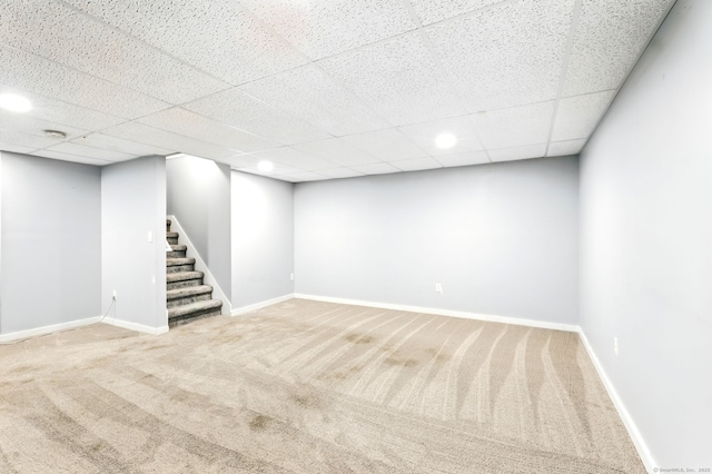 finished basement featuring baseboards, carpet flooring, a drop ceiling, and stairway