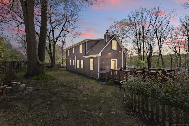 back of house at dusk featuring fence, a wooden deck, a chimney, and a yard