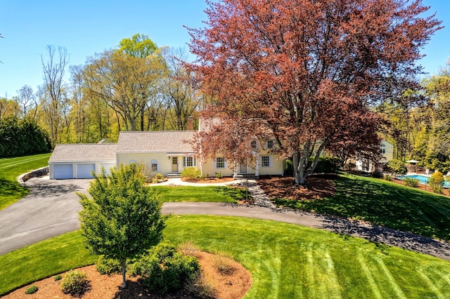 obstructed view of property featuring asphalt driveway, an attached garage, and a front yard