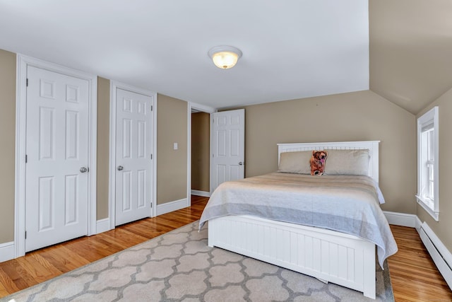 bedroom with a baseboard heating unit, wood finished floors, and baseboards