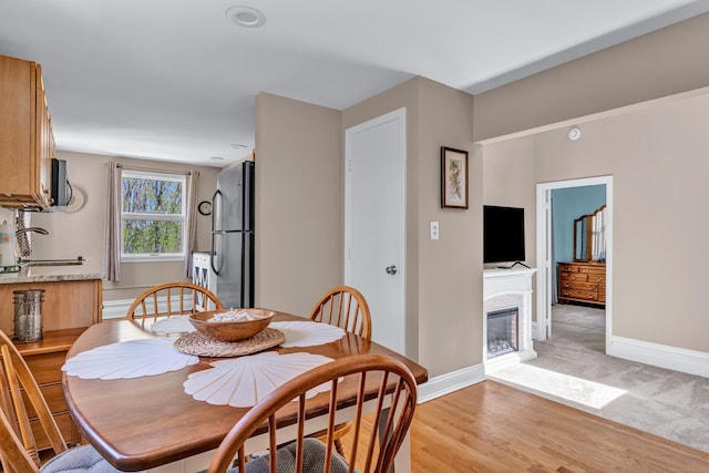 dining area featuring a glass covered fireplace, baseboards, and light wood-style flooring