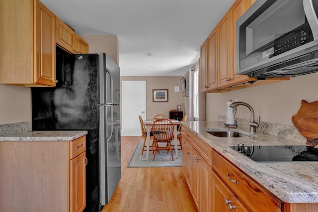 kitchen with stainless steel appliances, a sink, light wood-type flooring, and light stone countertops