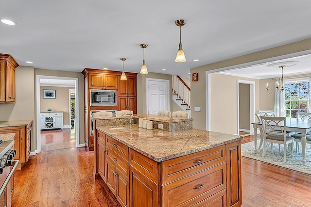 kitchen with black microwave, brown cabinets, wood finished floors, a sink, and recessed lighting