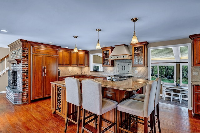 kitchen with custom range hood, paneled fridge, wood finished floors, backsplash, and a kitchen bar