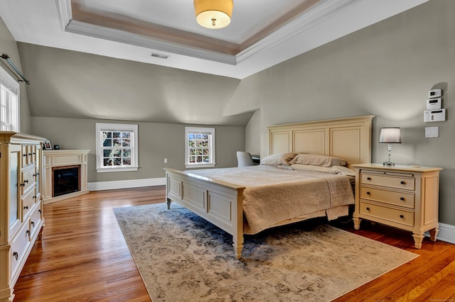 bedroom with multiple windows, wood finished floors, a raised ceiling, baseboards, and vaulted ceiling
