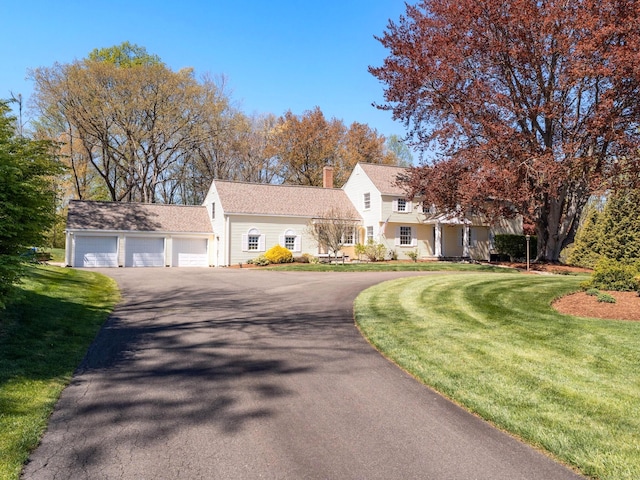 view of front of house featuring asphalt driveway, an attached garage, a front yard, and a chimney
