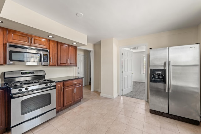 kitchen featuring baseboards, brown cabinetry, dark countertops, stainless steel appliances, and light colored carpet