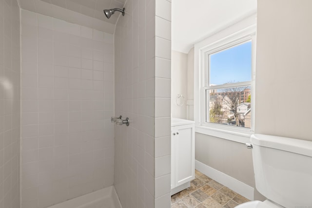 full bath featuring toilet, baseboards, tiled shower, and stone finish floor