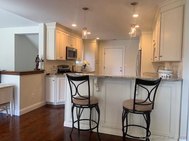 kitchen featuring white cabinets, a peninsula, appliances with stainless steel finishes, and decorative backsplash