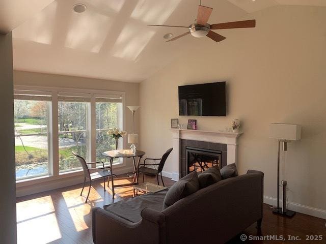 living area featuring lofted ceiling, a tile fireplace, ceiling fan, and baseboards