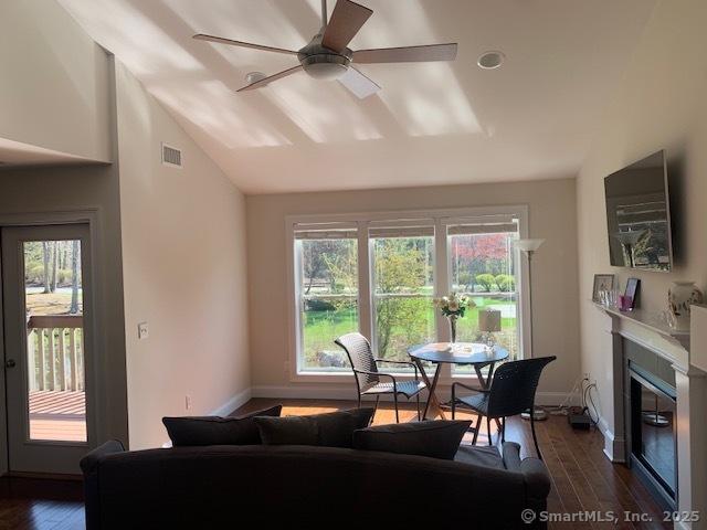 dining space with dark wood-style flooring, a glass covered fireplace, visible vents, a ceiling fan, and lofted ceiling