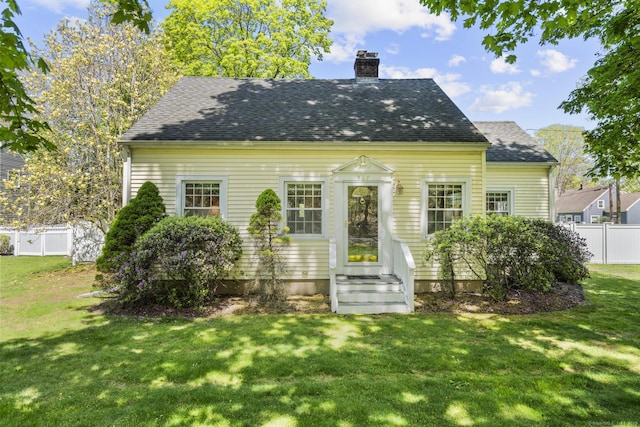 rear view of house featuring fence, a chimney, a lawn, and a shingled roof