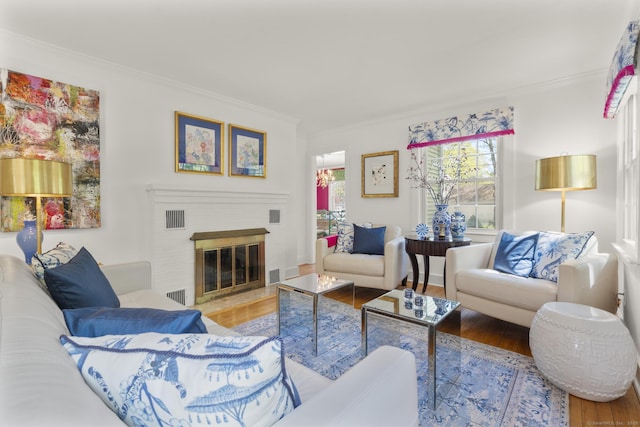 living area featuring visible vents, a brick fireplace, crown molding, and wood finished floors