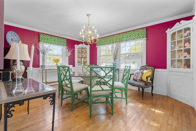 dining area with a healthy amount of sunlight, an inviting chandelier, ornamental molding, and hardwood / wood-style floors