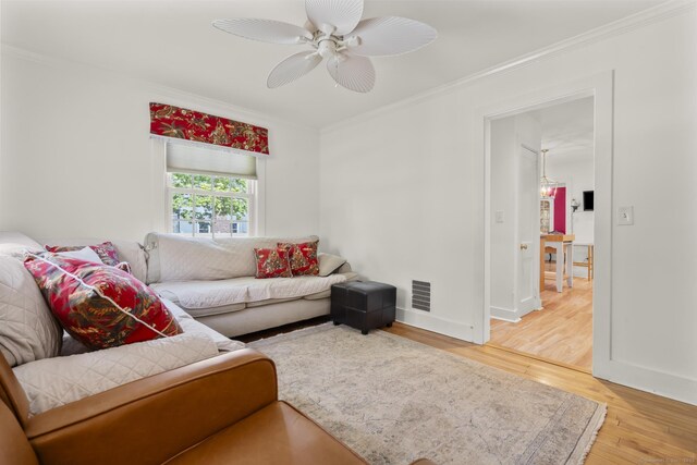 living room with light wood finished floors, a ceiling fan, baseboards, visible vents, and ornamental molding