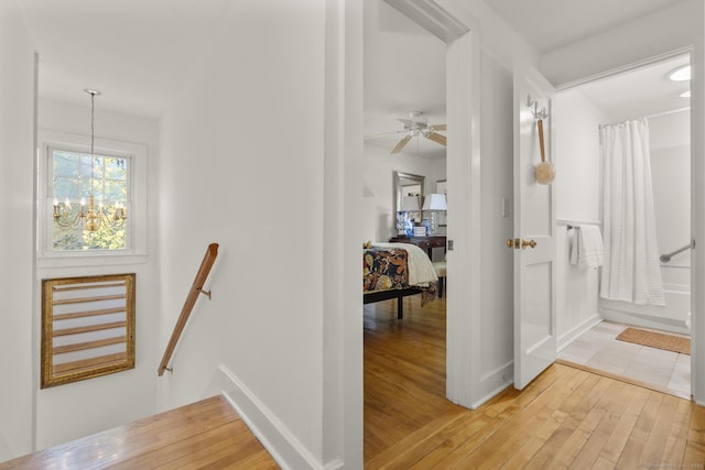 hallway featuring light wood-style floors, baseboards, a chandelier, and an upstairs landing