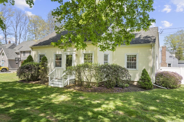 view of front of property with fence, a shingled roof, and a front lawn
