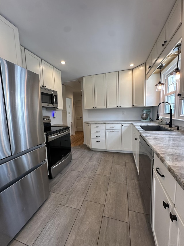 kitchen featuring appliances with stainless steel finishes, a sink, white cabinetry, wood finish floors, and recessed lighting