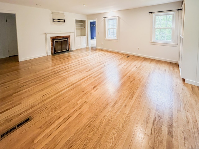 unfurnished living room with light wood-type flooring, healthy amount of natural light, a brick fireplace, and baseboards