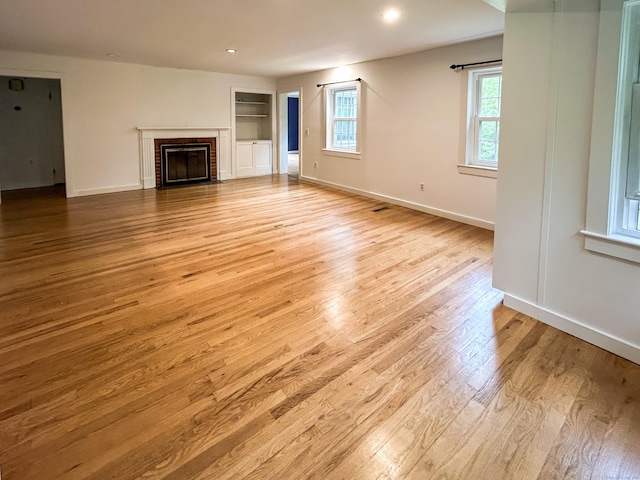 unfurnished living room with wood finished floors, baseboards, a brick fireplace, built in features, and recessed lighting