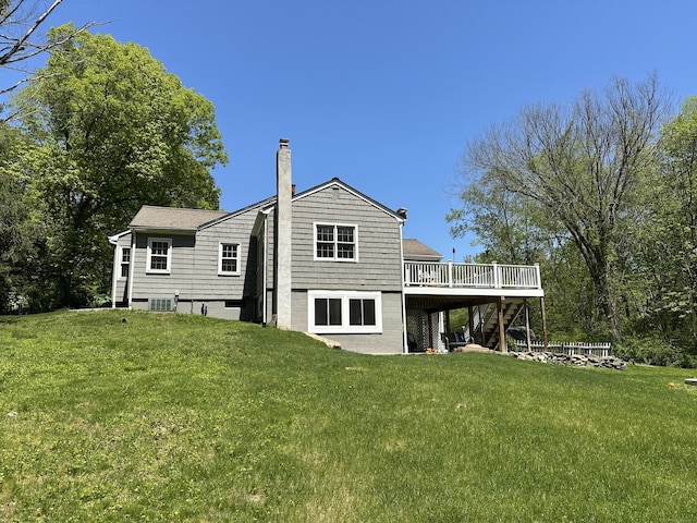 rear view of house with stairs, a deck, a chimney, and a lawn