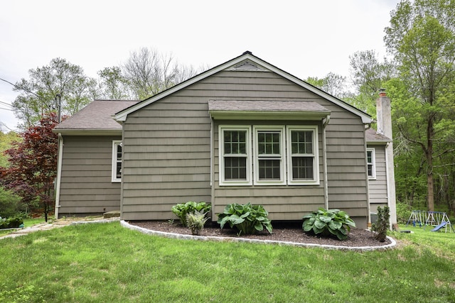 view of side of home with a yard, a shingled roof, a chimney, and a playground