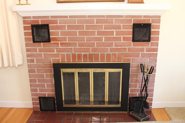 details with a brick fireplace, visible vents, wood finished floors, and baseboards