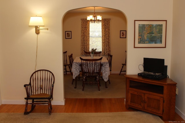 dining room featuring wood finished floors, baseboards, a notable chandelier, and arched walkways