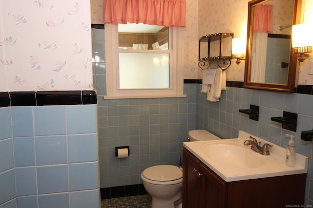 bathroom with tile walls, vanity, toilet, wainscoting, and wallpapered walls