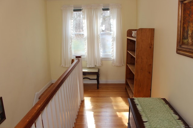 hallway with an upstairs landing, a healthy amount of sunlight, baseboards, and light wood-style floors