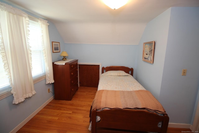 bedroom with lofted ceiling, light wood-type flooring, and baseboards