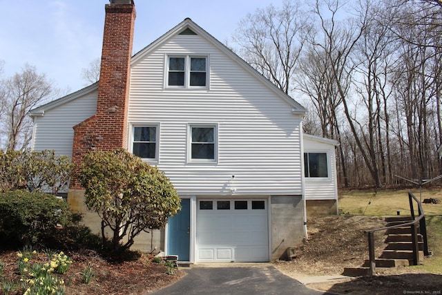 view of side of property featuring a garage, a chimney, and driveway