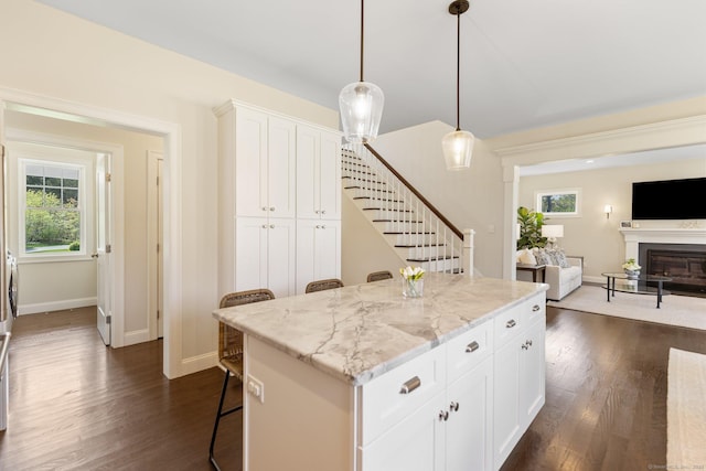 kitchen with dark wood-style flooring, light stone countertops, a center island, baseboards, and open floor plan