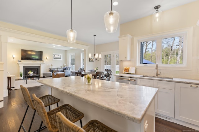 kitchen featuring a breakfast bar area, light stone countertops, dark wood finished floors, a sink, and white cabinetry