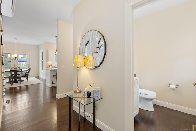hallway with baseboards, visible vents, dark wood finished floors, and an inviting chandelier