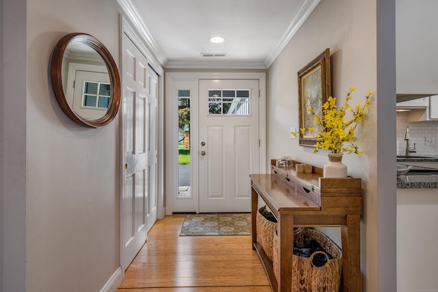 foyer entrance with visible vents, light wood-type flooring, and crown molding