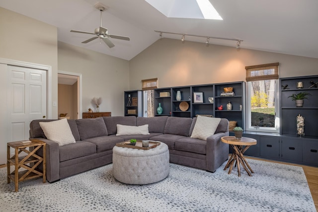 living area with ceiling fan, rail lighting, high vaulted ceiling, a skylight, and wood finished floors