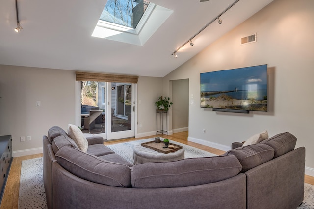 living room featuring vaulted ceiling with skylight, light wood-type flooring, visible vents, track lighting, and baseboards