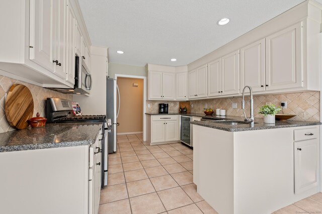 kitchen featuring stainless steel appliances, a peninsula, white cabinets, beverage cooler, and a sink