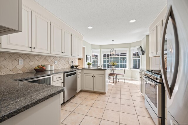 kitchen with appliances with stainless steel finishes, a peninsula, a sink, decorative backsplash, and white cabinets
