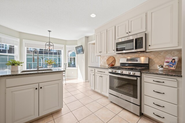 kitchen featuring appliances with stainless steel finishes, a sink, backsplash, a chandelier, and light tile patterned floors